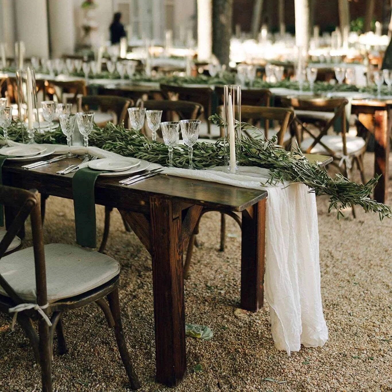 Styled farmhouse tables arranged in parallel rows with place settings, greenery, and cross back chairs
