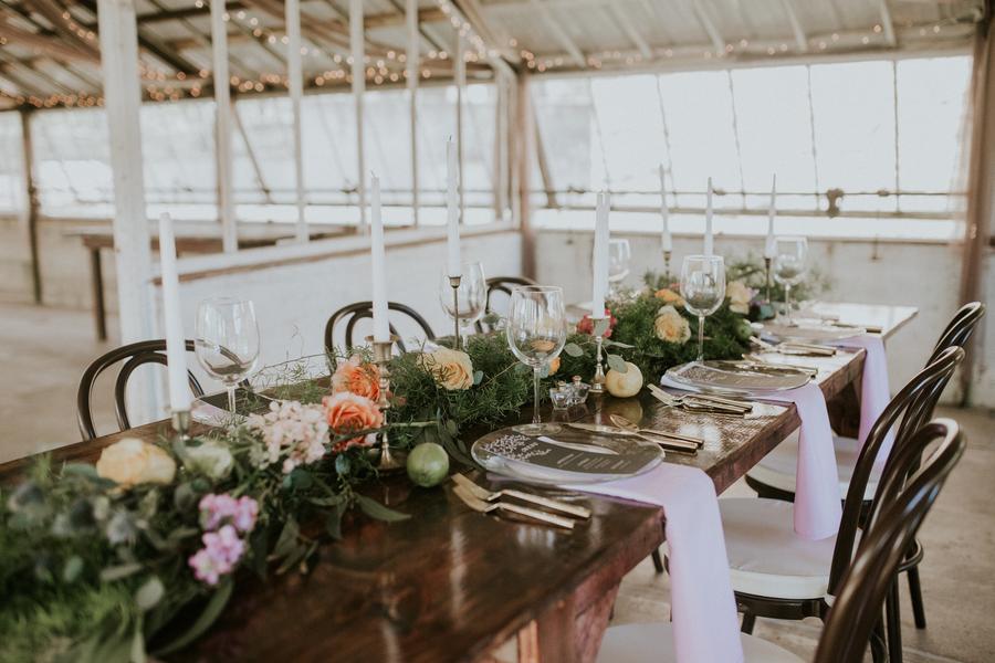 Decorated dining table with candles, flowers, glasses, and plates in a bright, industrial-style venue