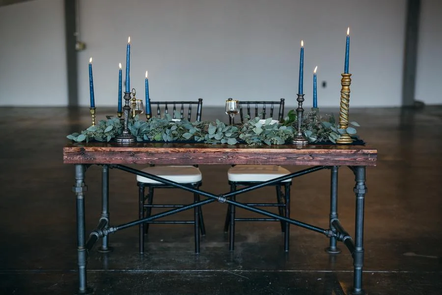 A dining table set with black chairs, decorated with greenery and blue candles in candle holders.