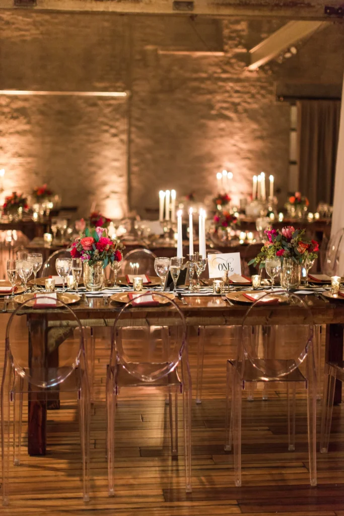 Elegant banquet table set with flowers, candles, glassware, and tableware in a warmly lit industrial-style venue.