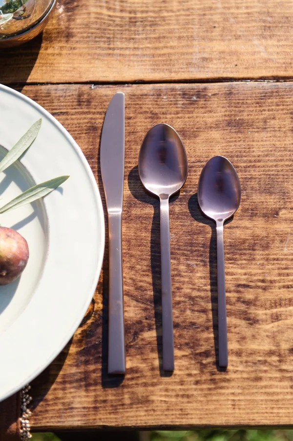 A set of three silver utensils, including a knife and two spoons, placed on a wooden table next to a white plate.