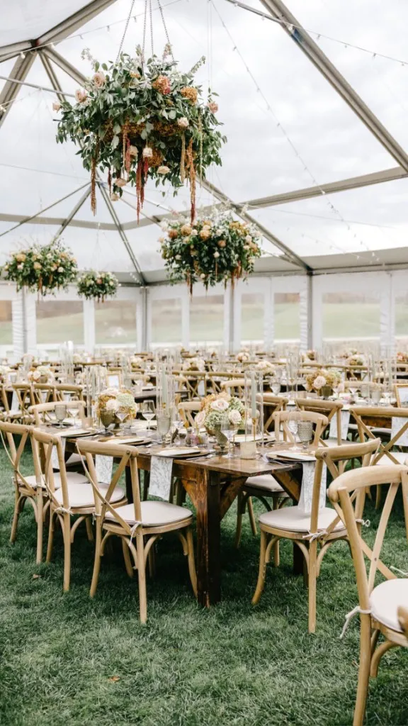 Clear-span tent reception with hanging floral chandeliers, farmhouse tables, and cross-back chairs