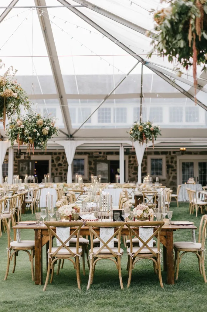 Close-up of a styled farmhouse table with cross-back chairs under a clear event tent
